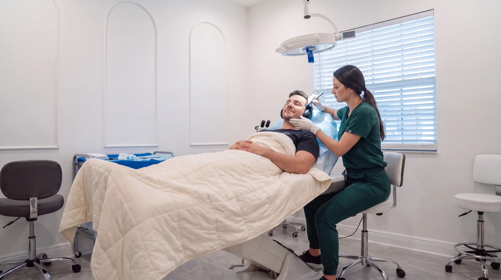 Patient reclined with headphones while his provider places grafts along his jawline, following the morning design